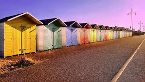 A row of colorful beach huts along a pebbled beach with a clear sky. - City Escape with a Touch of Class (Eastbourne)