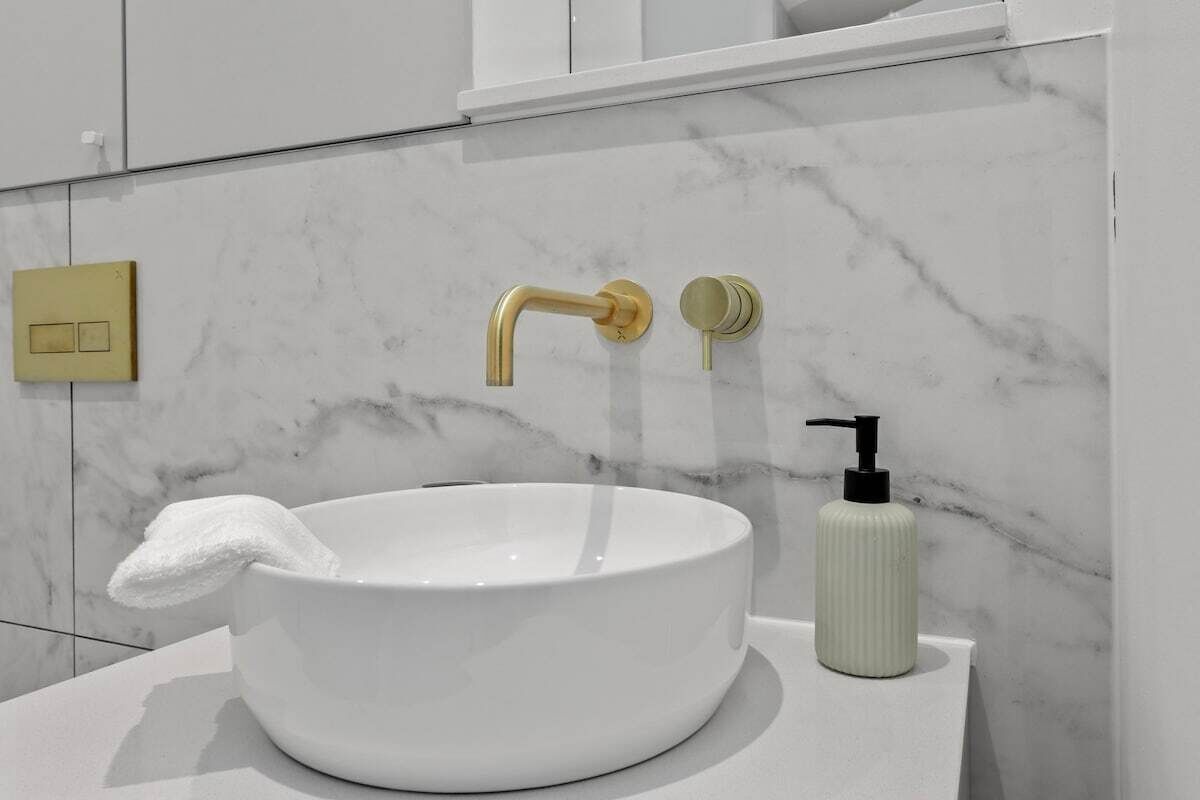 Ein Badezimmer mit einem weißen Marmorbecken, einem goldenen Wasserhahn und einer weißen Seifenspender.