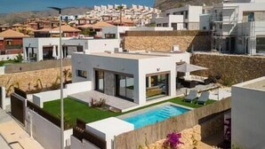 En modern villa med en swimmingpool, omgiven av ett bergigt landskap och andra moderna bostäder.