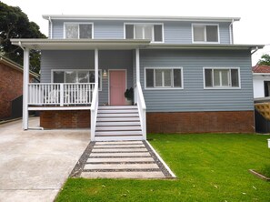 A two-story house with a front porch, a pink door, and a staircase leading to the entrance.