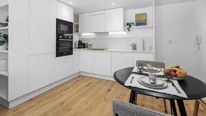 A modern kitchen with white cabinets, a black oven, and a dining table set with plates, glasses, and fruit. - Elevated Living in Eastbourne: Contemporary Gem (Eastbourne)