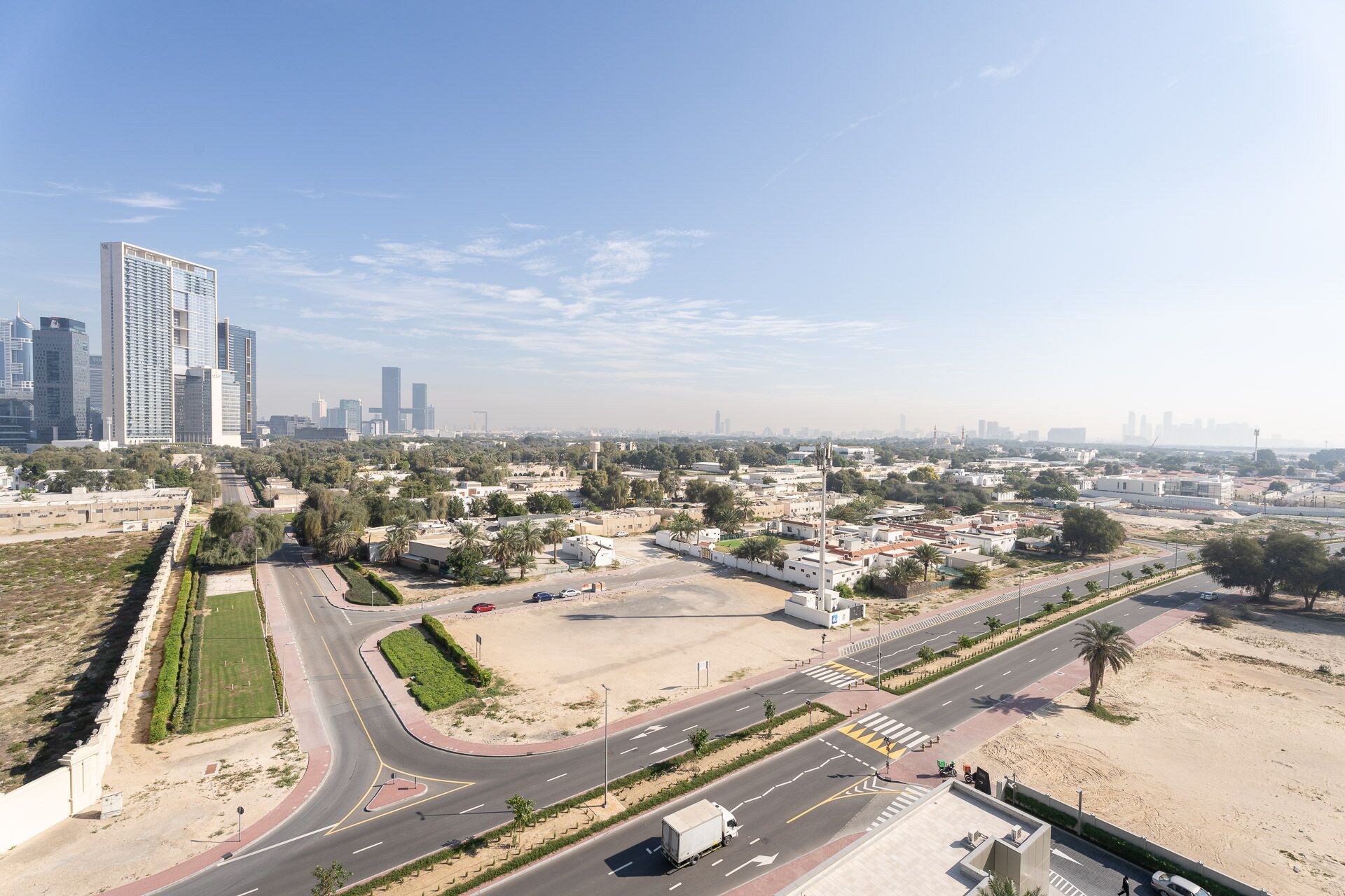 Un paysage urbain avec des immeubles modernes de grande hauteur, une large avenue et un mélange de zones résidentielles et commerciales.