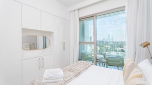Un dormitorio moderno con una cama grande, un espejo y vistas a la ciudad a través de una puerta corrediza de vidrio.