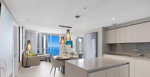 Una cocina moderna con una isla central, iluminación colgante y vista al océano.