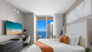 A modern hotel room with a large bed, a desk, a TV, and a balcony with a city view. - Endless Views | Oceanfront Balcony | Hot Tub (Hollywood)