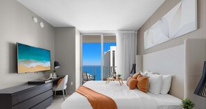 Una habitación de hotel moderna con una cama grande, un escritorio, televisión y un balcón con vista al océano.