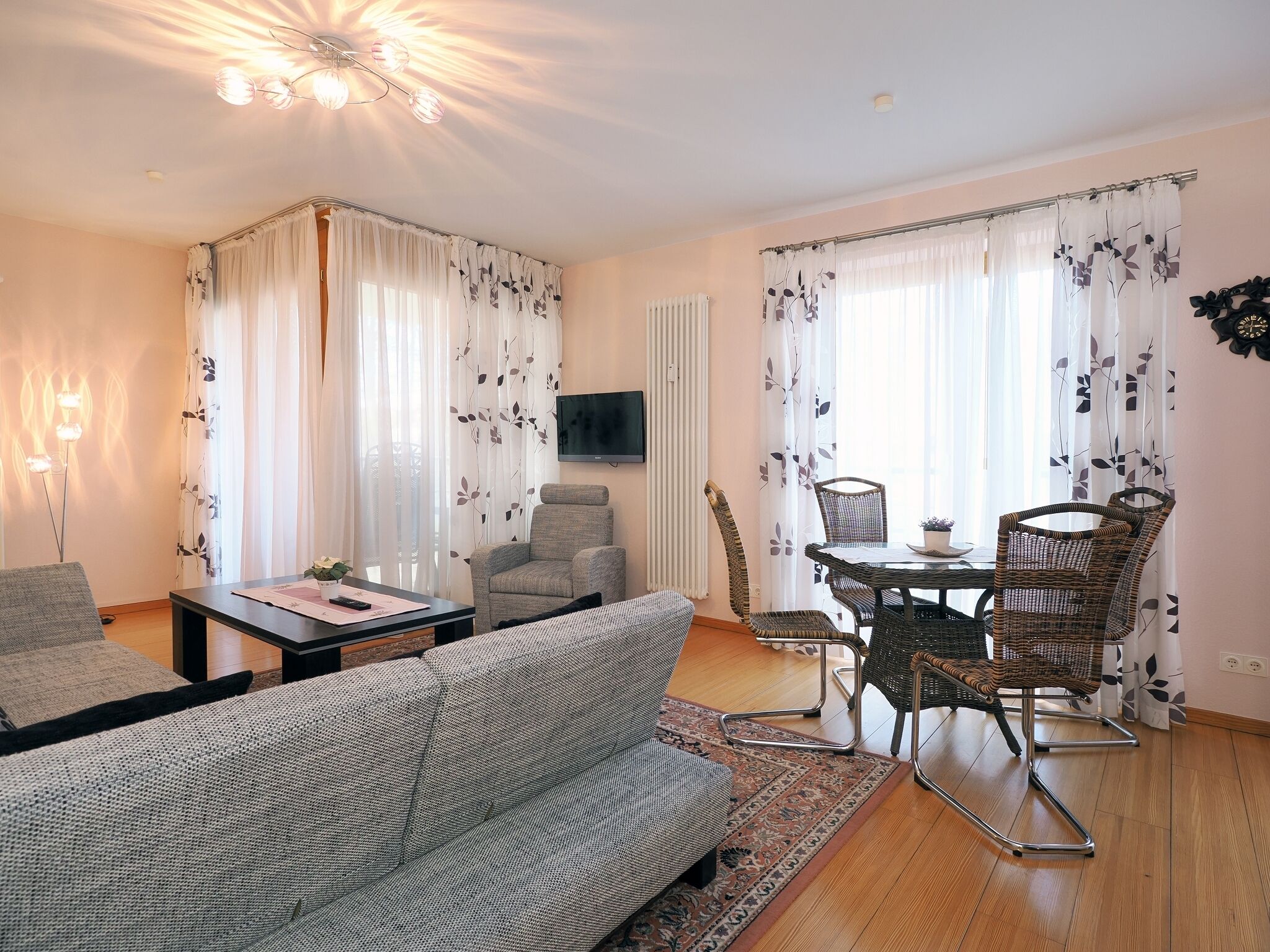 Un salon comprenant un canapé, une table à manger avec des chaises, un téléviseur fixé au mur et un radiateur.