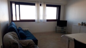 A living room with a sofa, a TV, a small table, and a window with curtains.