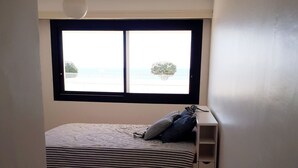 A small, single-bed room with a window overlooking a balcony.
