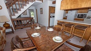 A dining area with a wooden table set for four, surrounded by leather chairs. A staircase is visible in the background, leading to another level. - 3336 Pine Hill Road 3 Bedroom Home (South Lake Tahoe)