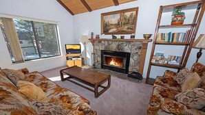 A living room with a fireplace, floral-patterned sofas, a coffee table, a bookshelf, and a television. - 3336 Pine Hill Road 3 Bedroom Home (South Lake Tahoe)