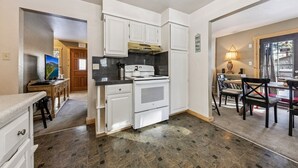 A compact kitchen with white cabinets, a stove, and a dining area with a table and chairs. - 750 Stanford Avenue 3 Bedroom Cabin by RedAwning (South Lake Tahoe)