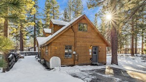 A wooden cabin with a snow-covered roof, surrounded by tall pine trees. - 750 Stanford Avenue 3 Bedroom Cabin by RedAwning (South Lake Tahoe)