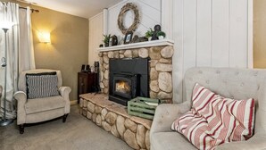 A cozy living room with a stone fireplace, two armchairs, a striped throw pillow, and a wall-mounted light fixture. - 750 Stanford Avenue 3 Bedroom Cabin by RedAwning (South Lake Tahoe)