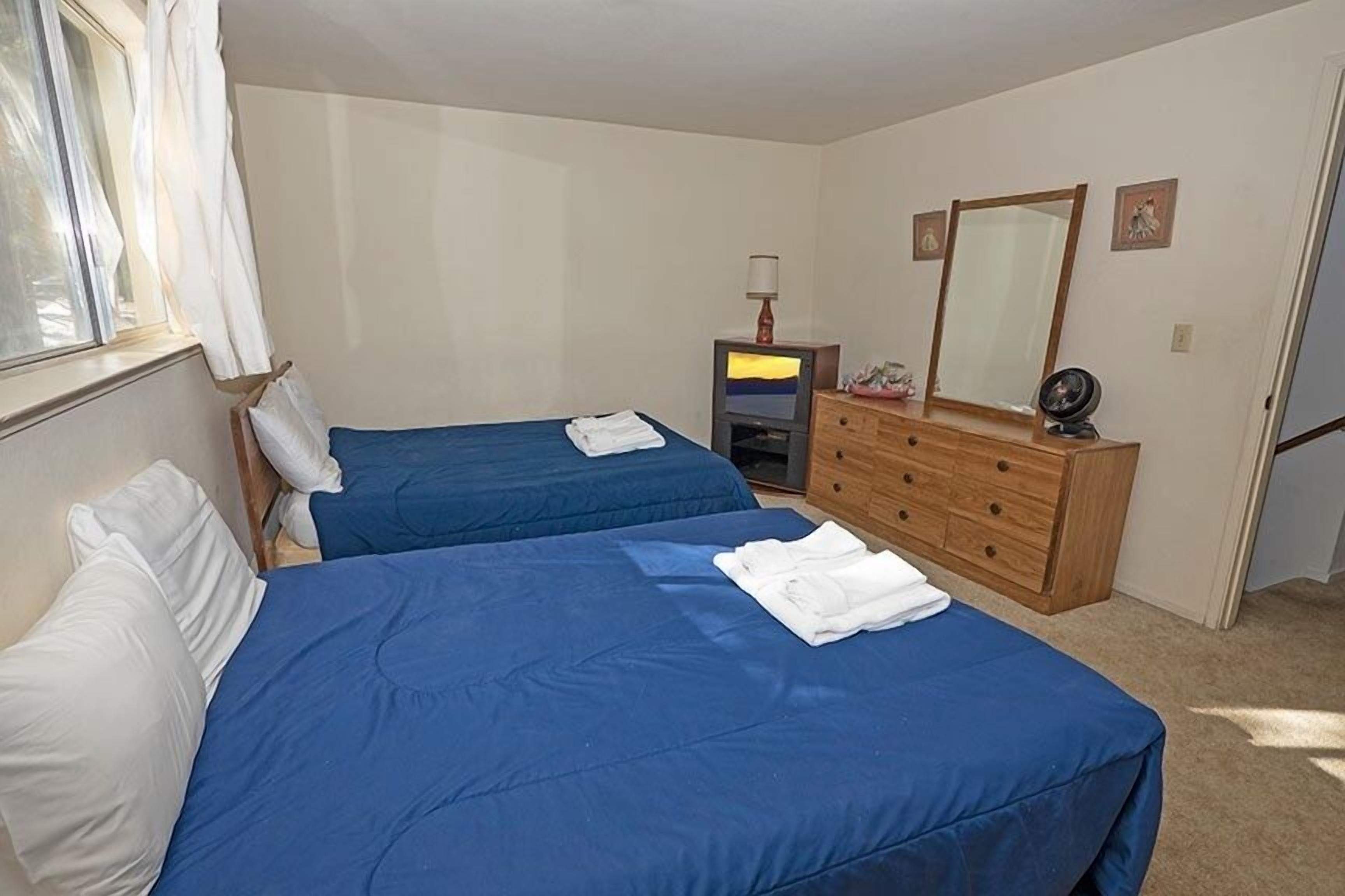 A bedroom with two beds, a dresser, a TV, and a mirror.