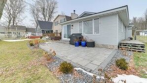 A residential house with a covered patio, a barbecue grill, and potted plants. - Bright Houghton Lake Home w/ Boat Dock + Fire Pit (Houghton Lake)