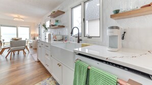 A modern kitchen with white cabinets, a large island, a coffee maker, and a view of the ocean. - Bright Houghton Lake Home w/ Boat Dock + Fire Pit (Houghton Lake)