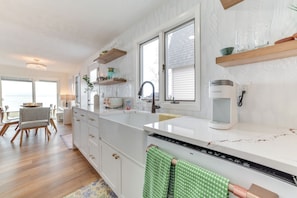 A modern kitchen with white cabinetry, a large island, and a view to the outside. - Bright Houghton Lake Home w/ Boat Dock + Fire Pit (Houghton Lake)