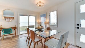 A modern dining area with a glass table, wooden chairs, and a chandelier. - Bright Houghton Lake Home w/ Boat Dock + Fire Pit (Houghton Lake)