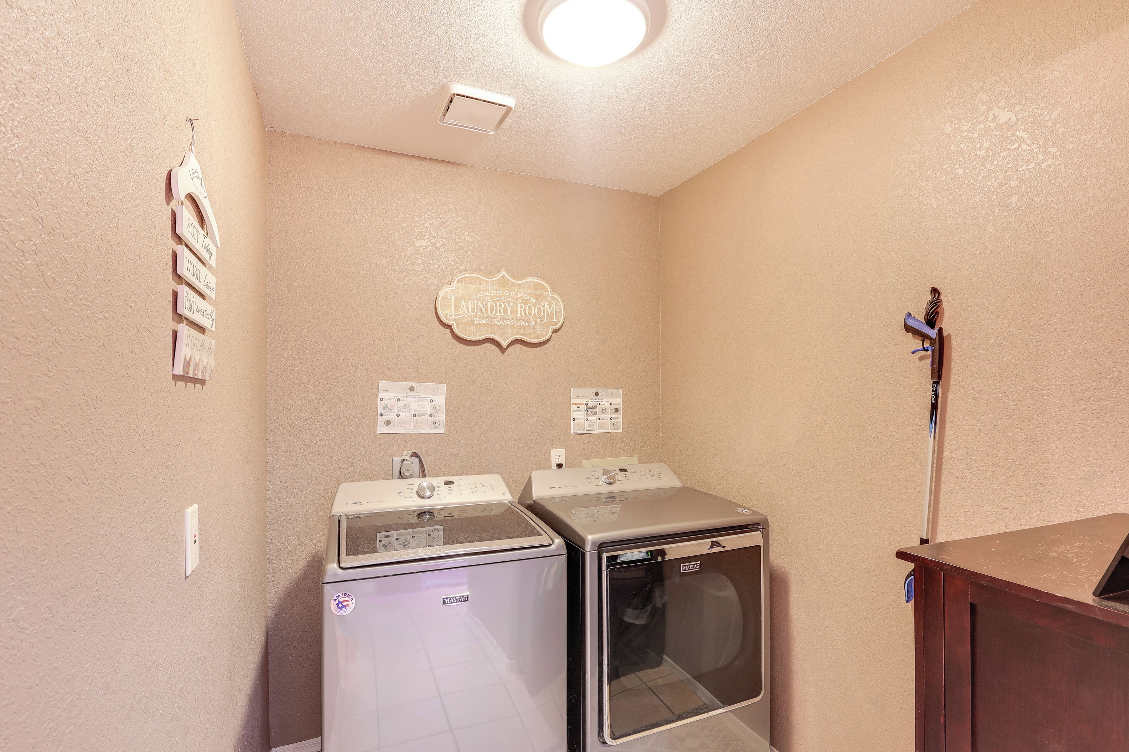 A laundry room with two washing machines and a dryer, a wooden cabinet, and a wall-mounted sign indicating the room's purpose.
