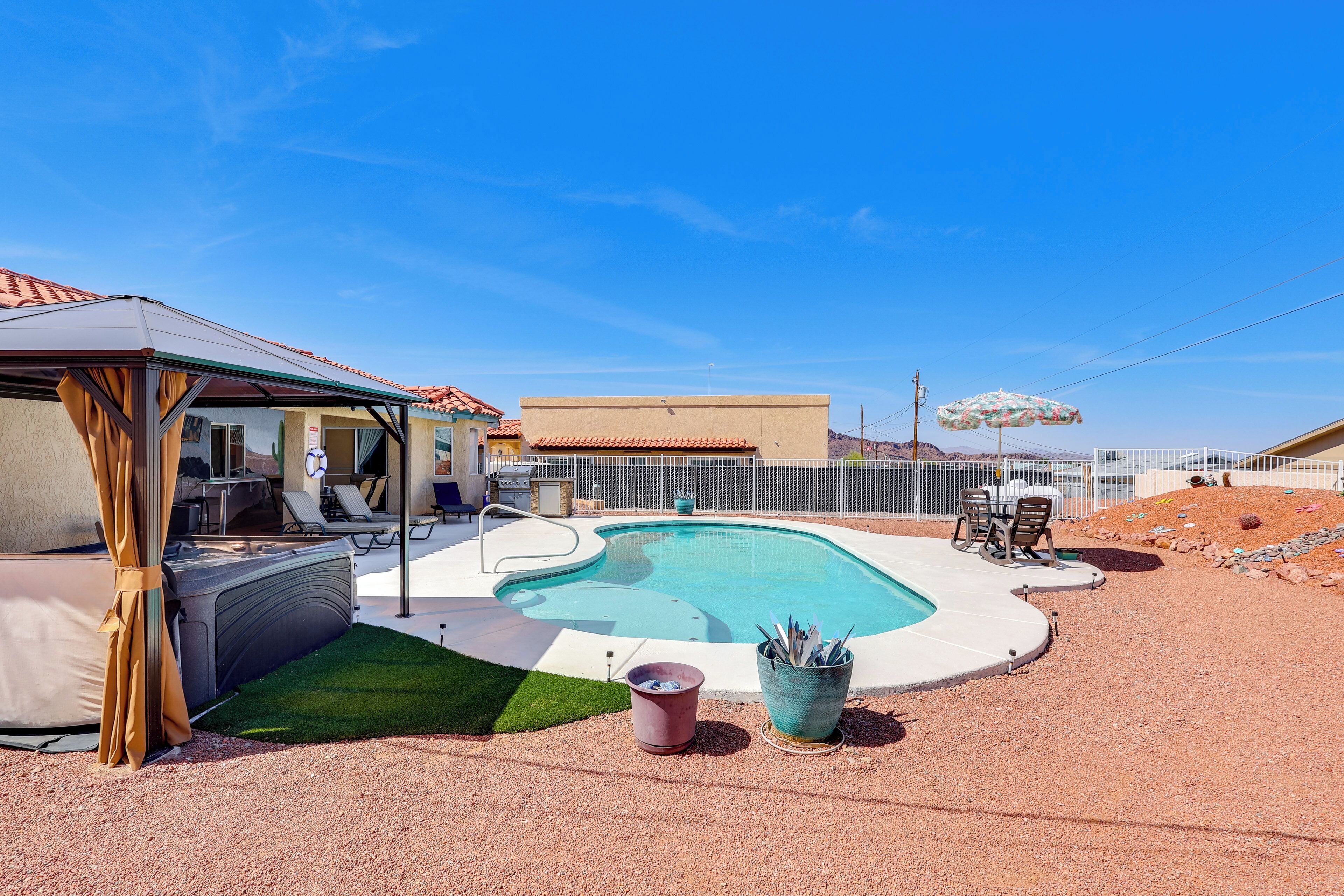 A swimming pool with a covered area, a hot tub, and a patio with chairs and a table.