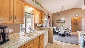 A kitchen with wooden cabinets, a coffee maker, and a dishwasher. There is a dining area with a table and chairs. - Cozy Lake Havasu City Home - Pool and Hot Tub (Lake Havasu City)