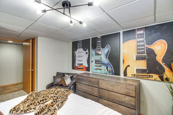 A bedroom with a bed, a dresser, and a wall with guitar posters.