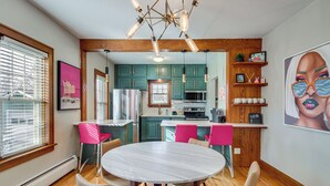A modern kitchen with teal cabinets, a white countertop, and a central island. There is a dining area with a round table and chairs. - Spacious Detroit Lakes Home: Walk to Downtown! (Detroit Lakes)