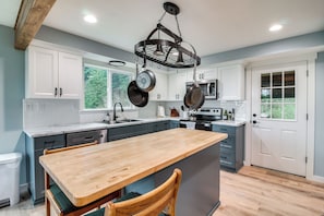 A modern kitchen with white cabinets, a wooden island, and hanging pots. - 3 Mi to Reedsport: Home w/ Umpqua River Views (Reedsport)