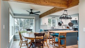 A modern kitchen with wooden beams, a dining area with a round table and chairs, and a view through large windows. - 3 Mi to Reedsport: Home w/ Umpqua River Views (Reedsport)
