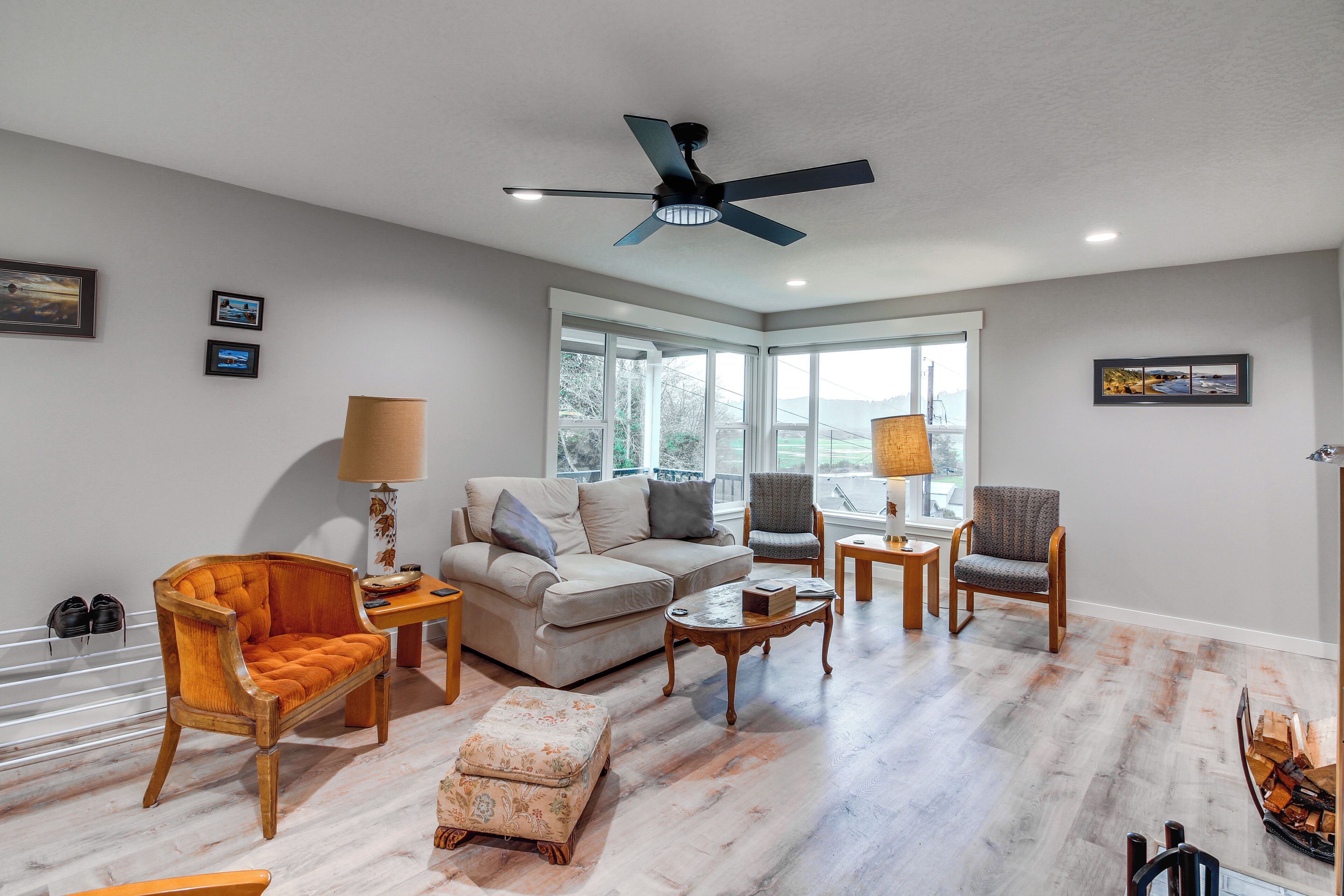 A spacious living room with a large window, a ceiling fan, and a variety of seating options including a sofa, chairs, and an ottoman.