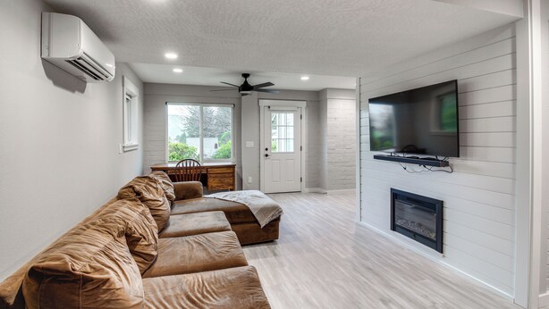 A modern living room with a sofa, TV, fireplace, and a ceiling fan. - 3 Mi to Reedsport: Home w/ Umpqua River Views (Reedsport)