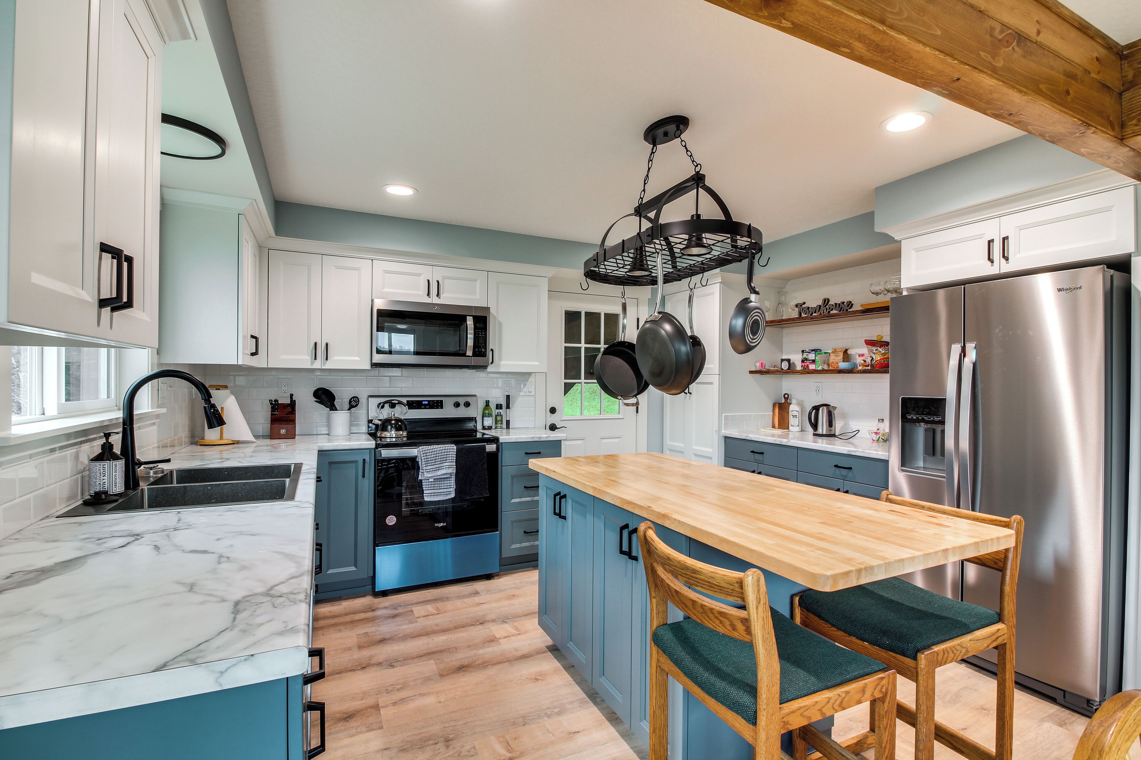 A modern kitchen with white cabinets, a wooden island, a stainless steel refrigerator, and a hanging pot rack.