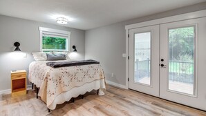 A bedroom with a bed, bedside lamps, a window, and a door leading to an outdoor area. - 3 Mi to Reedsport: Home w/ Umpqua River Views (Reedsport)