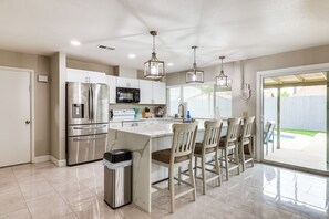 A modern kitchen with stainless steel appliances, a marble island, and wooden chairs. - Backyard Oasis! Family-friendly Tempe Retreat (Tempe)