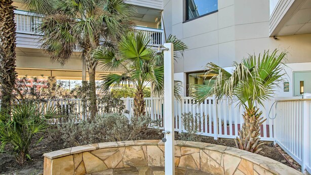 A courtyard with a stone bench, palm trees, and a white fence. - Galveston Condo w/ Beach Access Near Moody Gardens (Galveston)