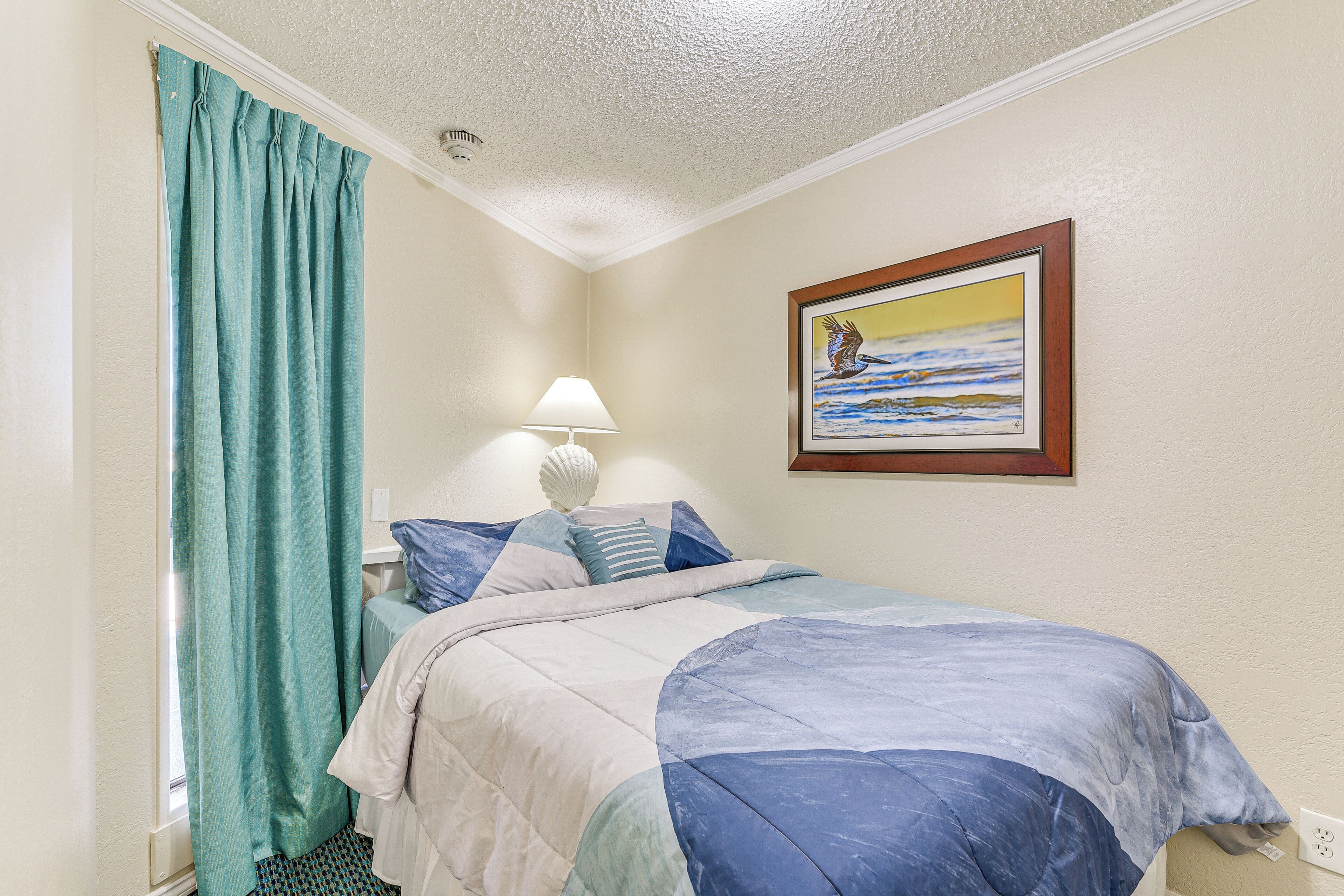 A bedroom with a bed, a nightstand, a lamp, a painting on the wall, and a window with curtains.