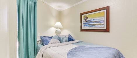 A bedroom with a bed, a nightstand, a lamp, a painting on the wall, and a window with curtains.