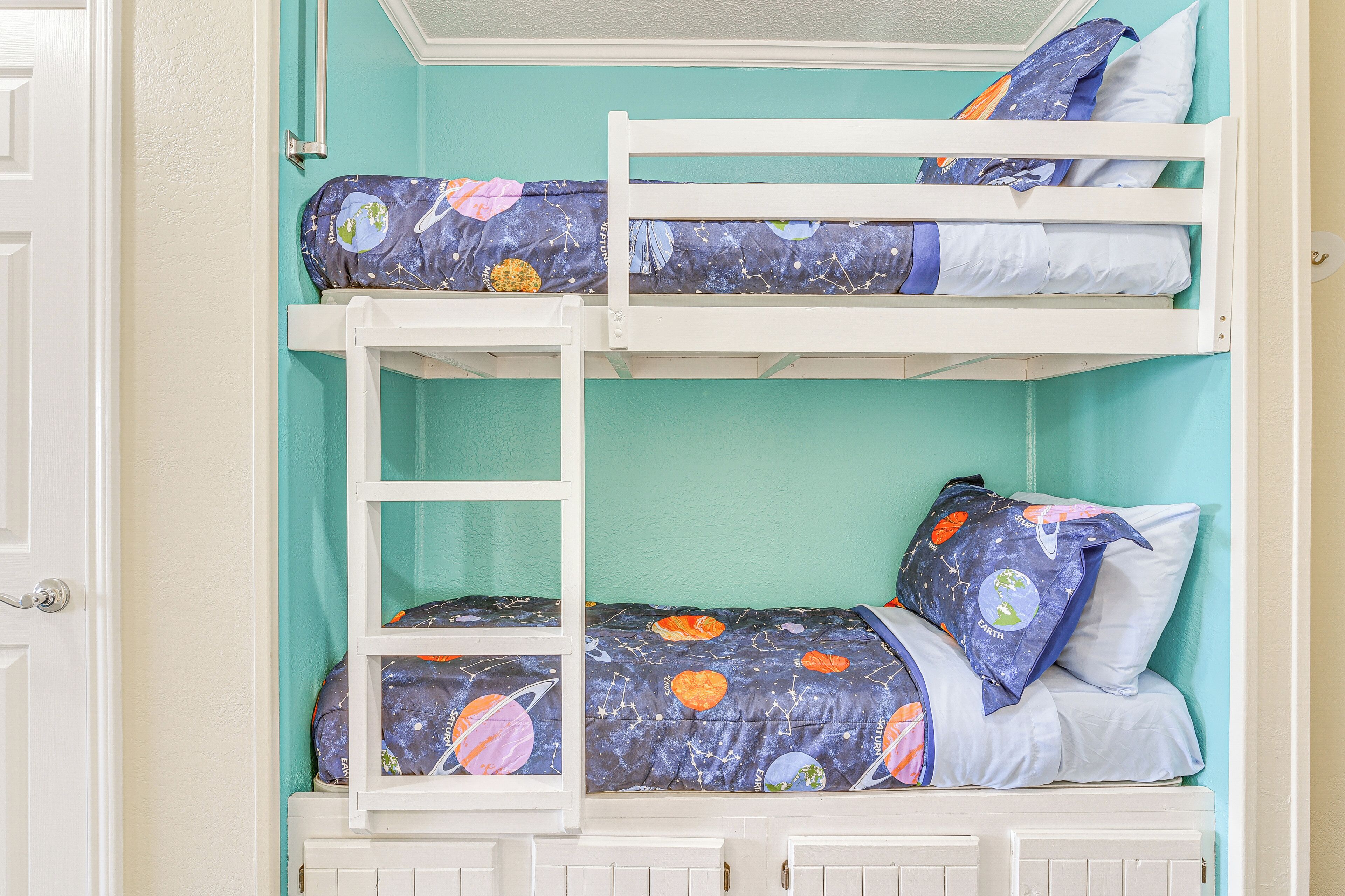 A bunk bed with a galaxy-themed bedspread and pillows, set against a teal wall.