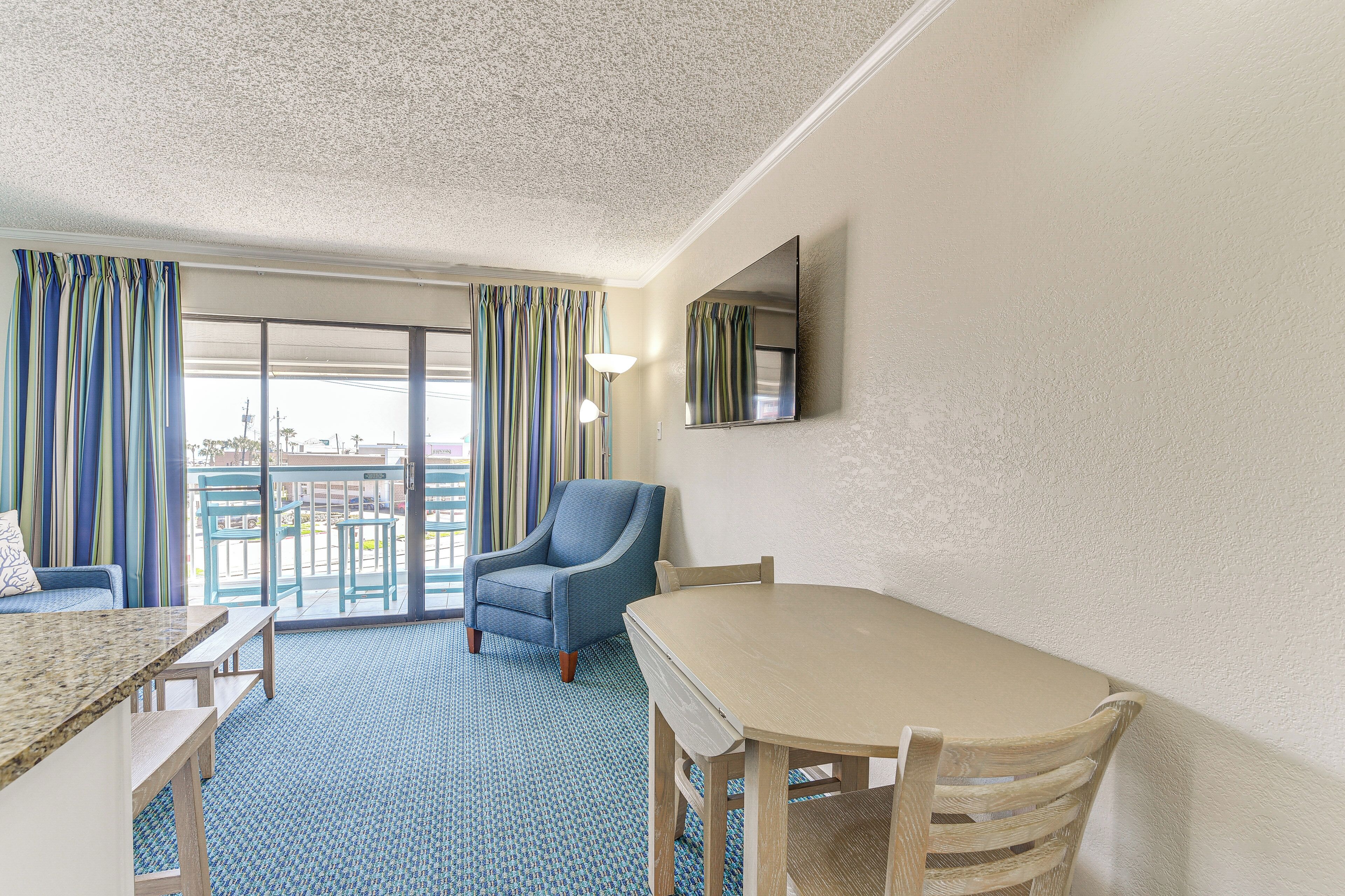 A hotel room with a large window, a chair, a table, and a view of the city.
