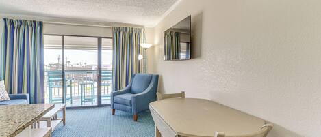 A hotel room with a large window, a chair, a table, and a view of the city.