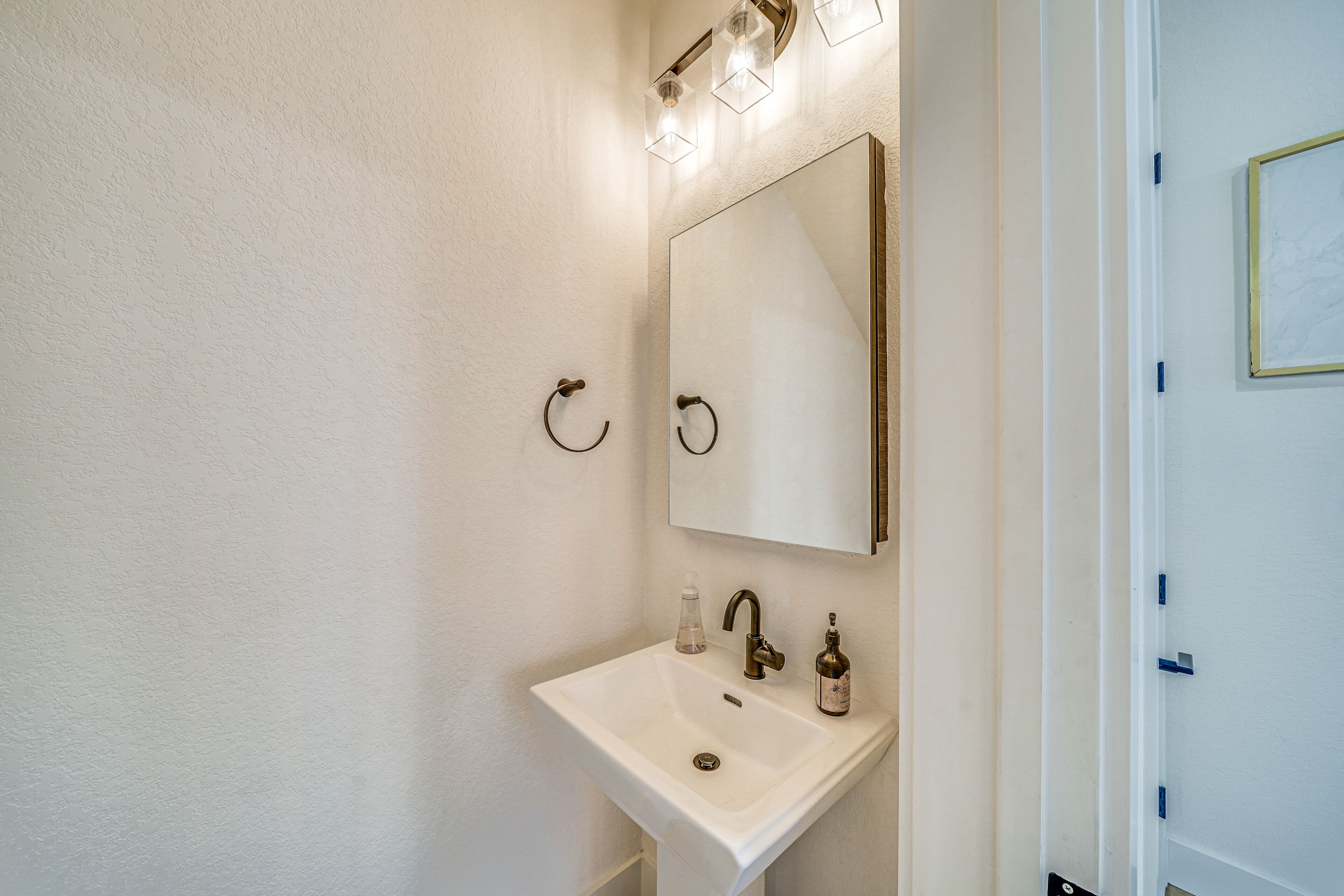 Un baño con lavamanos blanco, un espejo y una lámpara sobre el espejo.