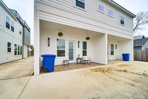 A two-story house with a covered porch, a small table, two chairs, and two trash bins.