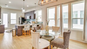 Una cocina moderna con armarios de madera oscura, una isla central y un comedor con mesa de vidrio y sillas tapizadas.