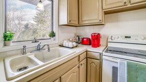 A kitchen with a double sink, a stove, cabinets, a window with plants, and a red coffee maker.