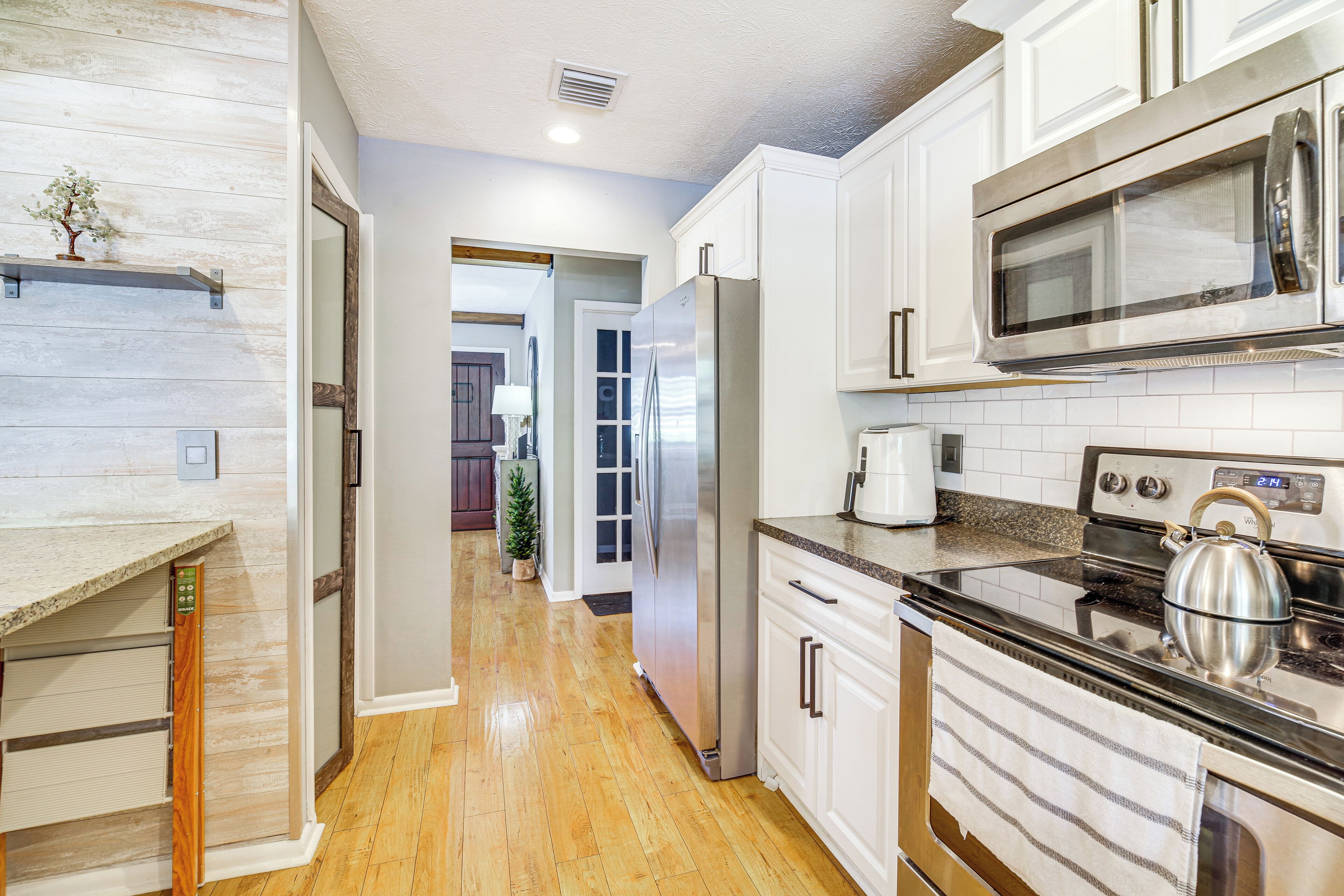 A modern kitchen with white cabinets, stainless steel appliances, and a wooden floor.