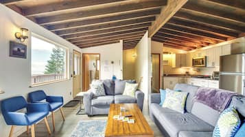 A modern living room with a wooden ceiling, grey sofas, blue chairs, and a wooden coffee table.
