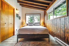 Un dormitorio con estructura de cama de madera, un ventanal con vistas a árboles y paneles de pared de madera.