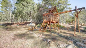 A wooden play structure in a natural setting with trees and rocks. - Mtn Views + Playground: Family-friendly Pine Cabin (Pine)