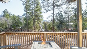 A deck with a fire pit, wooden railings, and a view of trees and mountains. - Mtn Views + Playground: Family-friendly Pine Cabin (Pine)